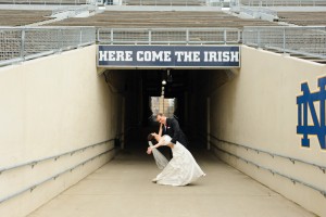 elegant bride and groom dipping under here come the irish sign on the notre dame football field